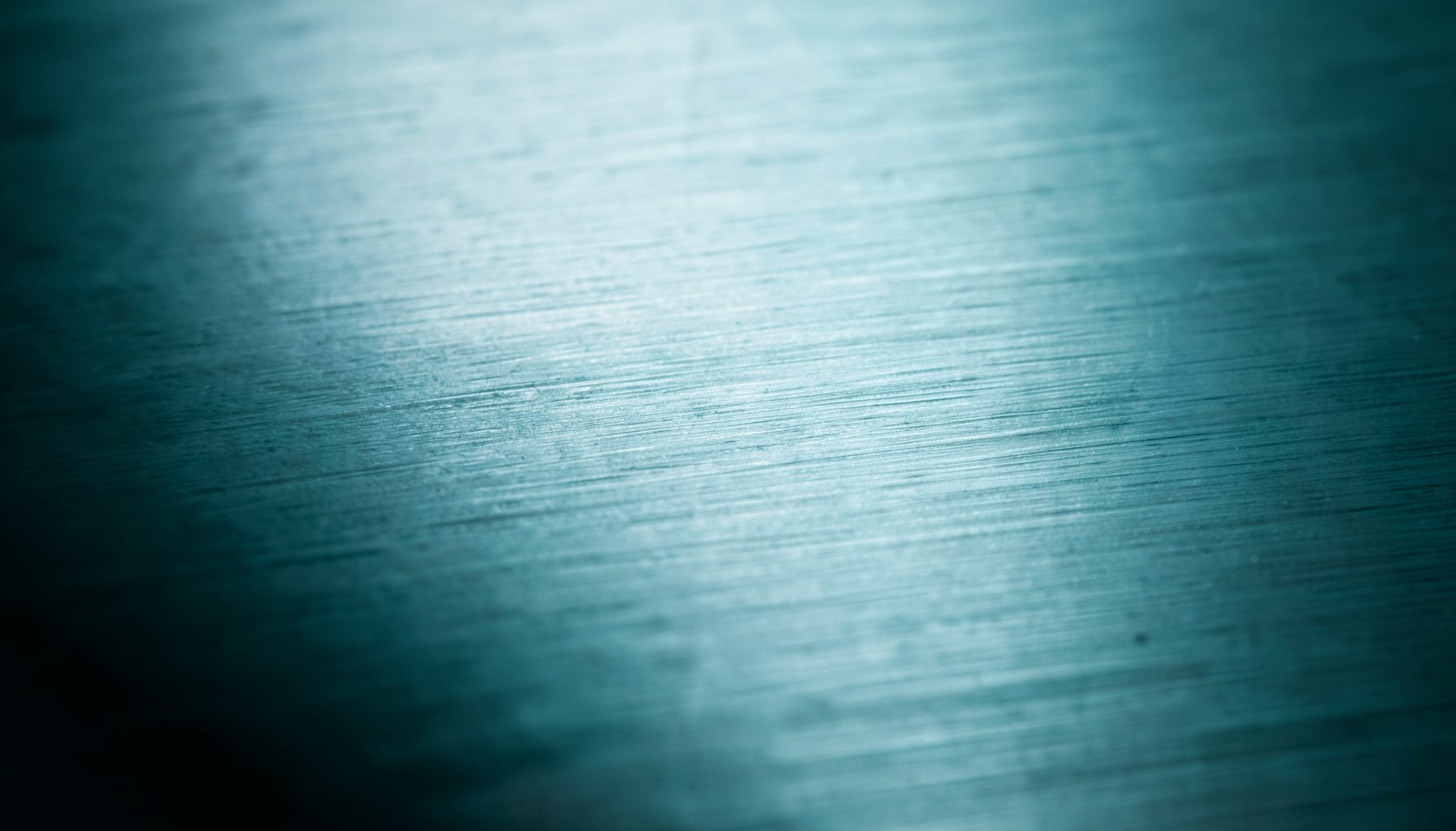 Close-up of brushed aluminum surface with subtle horizontal grain lines, cool silver-gray tones fading into dark shadow at edges, industrial and sleek mood.